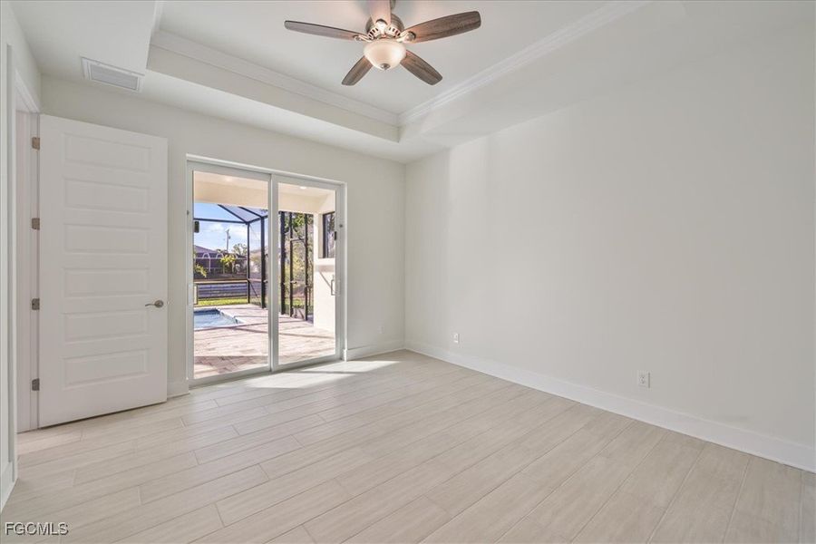 Empty room featuring a sunroom, a tray ceiling, ceiling fan, light wood-type flooring, and ornamental molding