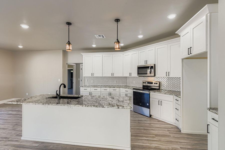 Kitchen featuring appliances with stainless steel finishes, pendant lighting, light stone countertops, an island with sink, and decorative backsplash