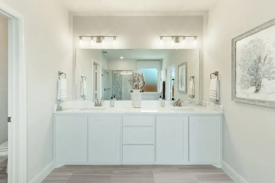 Bathroom with double vanity, white cabinets, marble countertops, and large mirror with overhead lighting