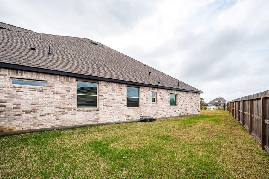 This photo shows the side view of a brick house with a sloped roof and several windows. It features a fenced grassy yard, ideal for outdoor activities and privacy. This photo shows the side view of a brick house with a sloped roof and several windows. It features a fenced grassy yard, ideal for outdoor activities and privacy.