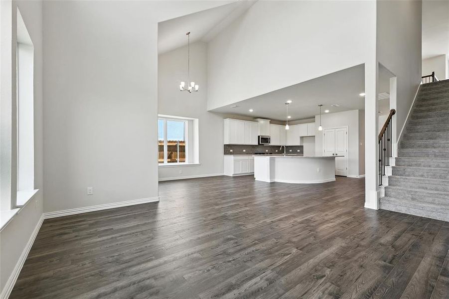 Unfurnished living room with suspended lighting, dark wood-type flooring, and vaulted ceiling