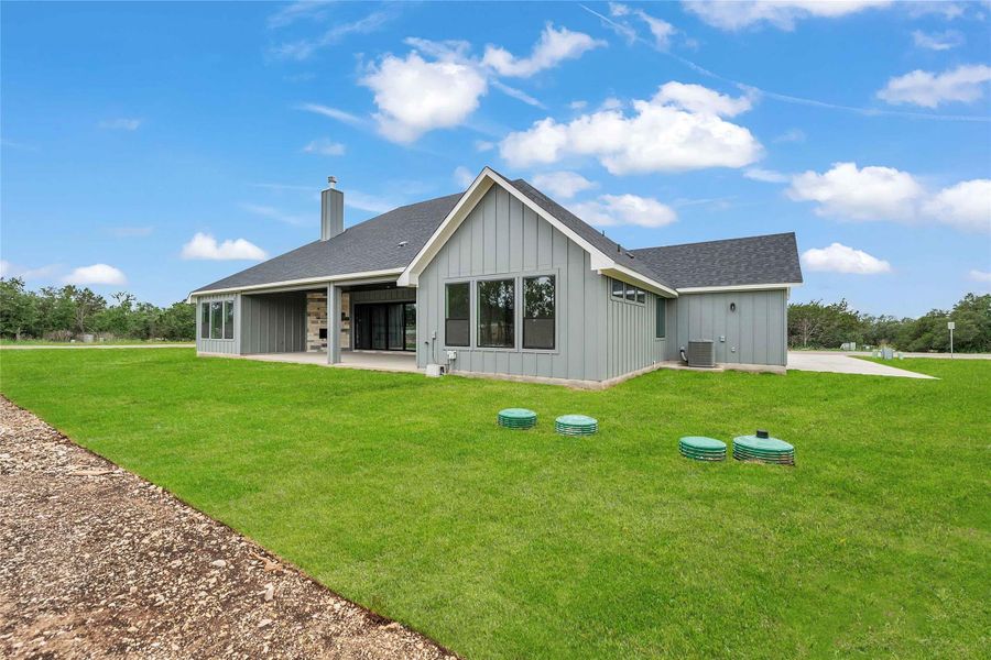 Rear view of house featuring a patio, board and batten siding, a lawn, and a chimney Rear view of house featuring a patio, board and batten siding, a lawn, and a chimney