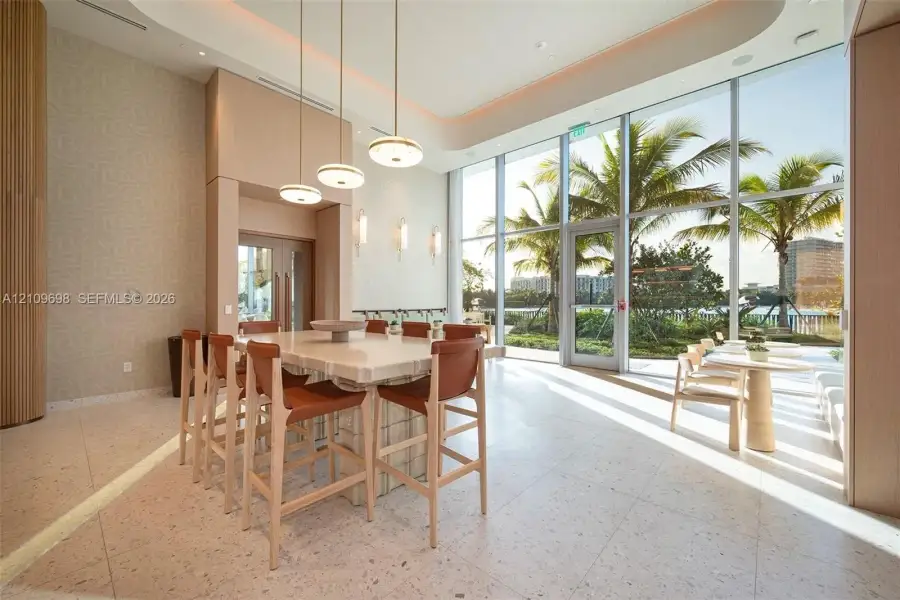 Floor-to-ceiling windows, stone-finish tile flooring, recessed tray ceiling, pendant lighting, and a built-in stone island