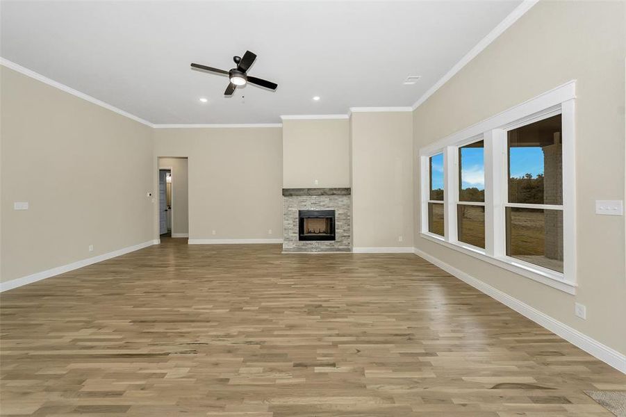 Unfurnished living room featuring a fireplace, ceiling fan, crown molding, and light wood-type flooring