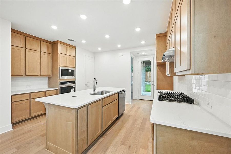 Kitchen featuring backsplash, a center island with sink, recessed lighting, light wood-style flooring, and light stone counters Kitchen featuring backsplash, a center island with sink, recessed lighting, light wood-style flooring, and light stone counters