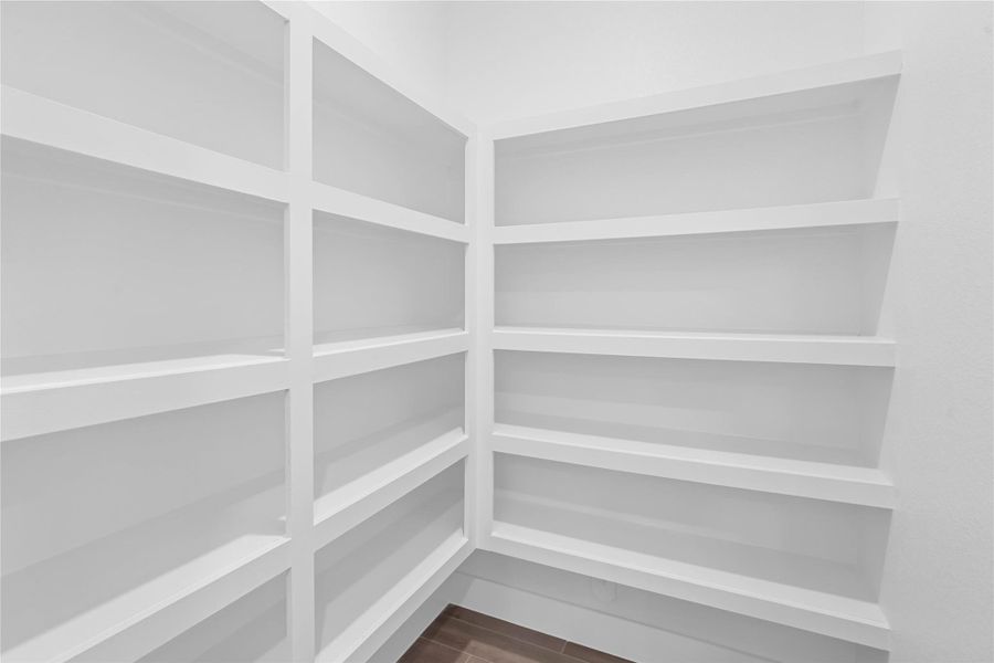 Spacious walk-in pantry offers exceptional storage potential, featuring multiple tiers of sturdy, built-in white shelving. Designed for maximum organization, the deep shelves provide ample space for all your culinary needs.