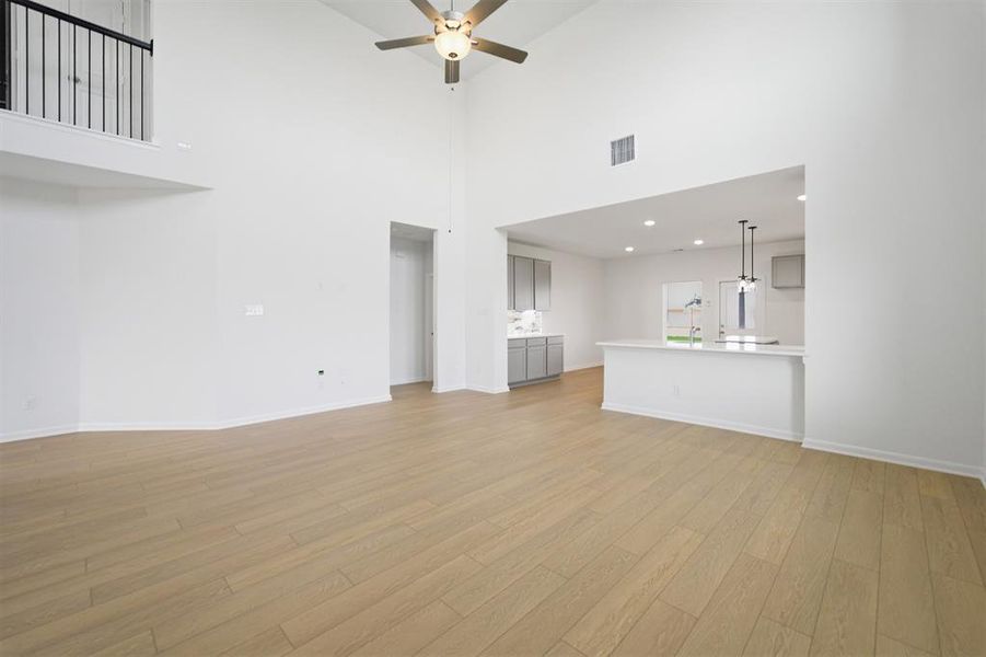 Unfurnished living room with a ceiling fan, light wood-style floors, recessed lighting, and a high ceiling