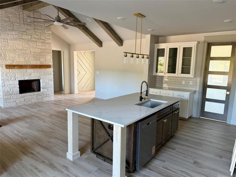 Kitchen with glass insert cabinets, white cabinetry, an island with sink, a ceiling fan, and light wood finished floors