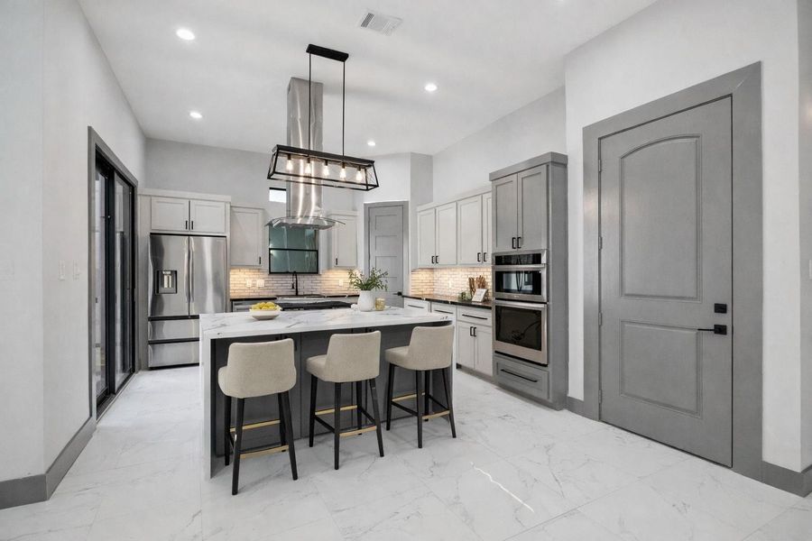 Custom cabinetry pairs seamlessly with a large waterfall island and stainless steel appliances. Sleek vent hood and statement lighting create a strong focal point, while the subway tile backsplash and under-cabinet lighting bring in timeless detail. *Virtually staged* Custom cabinetry pairs seamlessly with a large waterfall island and stainless steel appliances. Sleek vent hood and statement lighting create a strong focal point, while the subway tile backsplash and under-cabinet lighting bring in timeless detail. *Virtually staged*