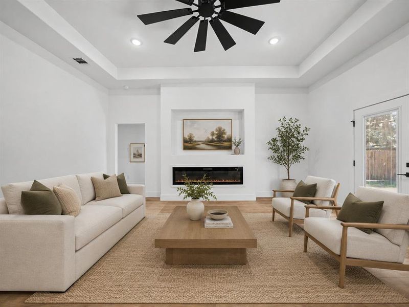 Spacious living area featuring high tray ceilings, recessed lighting, and wood-finish flooring Spacious living area featuring high tray ceilings, recessed lighting, and wood-finish flooring