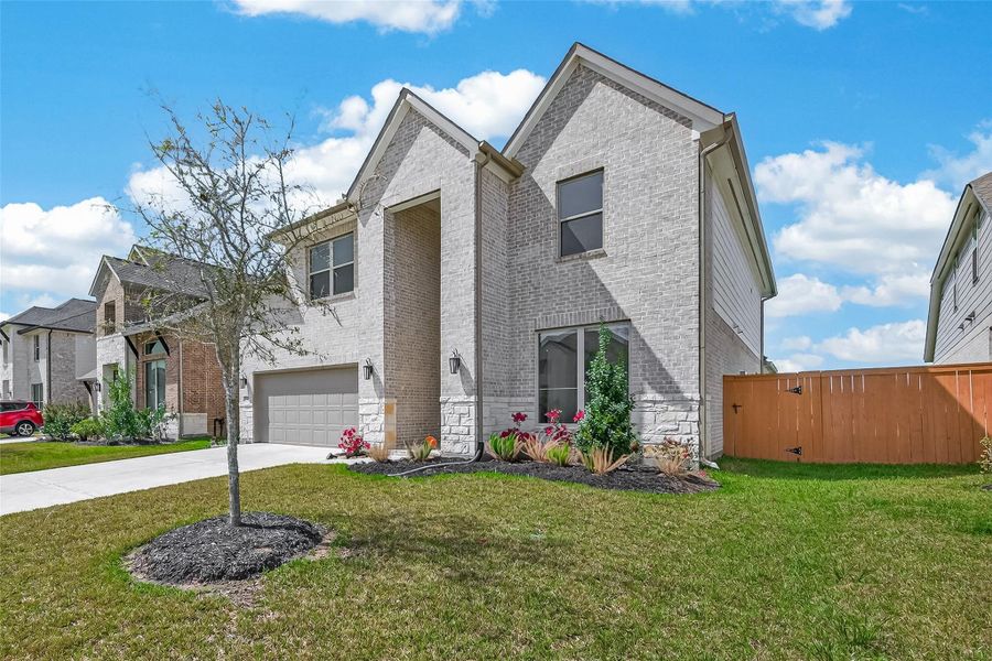 This photo showcases a modern two-story brick home with a well-kept front yard and simple landscaping. It features a two-car garage and a wooden fence, offering a blend of style and privacy.