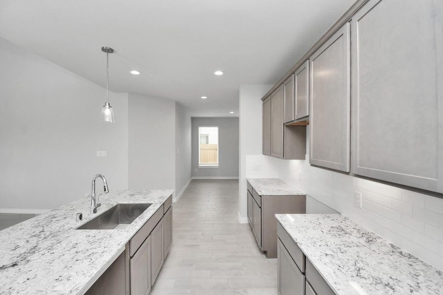 Step into the dream kitchen you've always wanted! This generously spacious culinary haven features a massive granite island, high ceilings, soft-close cabinets, granite countertops, stainless steel appliances, a sleek tile backsplash, and recessed lighting. Sample photo of completed home with similar floor plan. Actual colors and selections may vary.