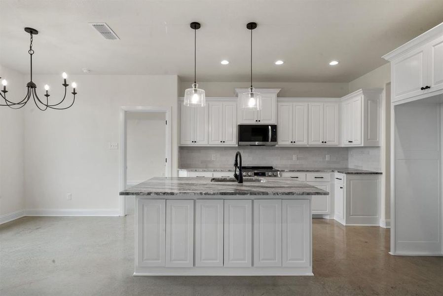 Kitchen with white cabinetry, light stone countertops, sink, and an island with sink