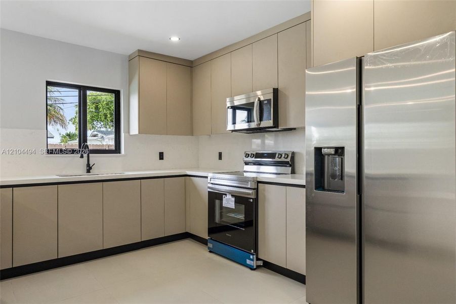 Kitchen featuring flat-panel cabinetry, quartz countertops, stainless steel appliances, and a matte black faucet