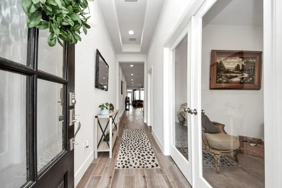 A welcoming hallway greets you with warm wood flooring, thoughtfully curated décor, and soft recessed lighting that creates an inviting ambiance. Elegant glass doors open into a cozy sitting area, while the stylish runner adds a touch of personality and charm to the space.