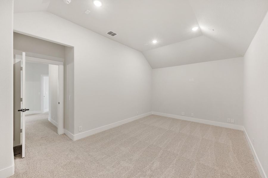 Empty bedroom with vaulted ceiling, beige carpet, and white walls with recessed lighting