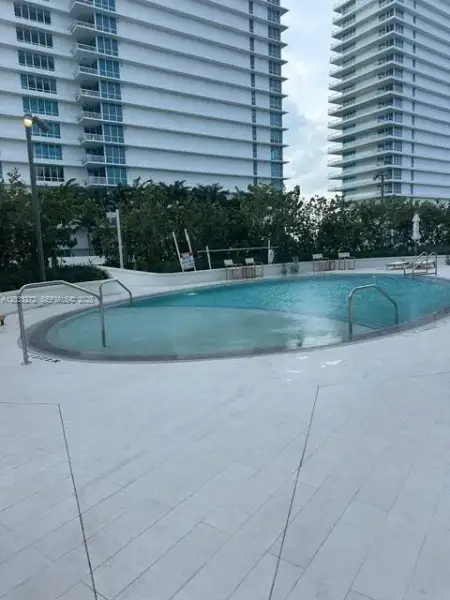 Oval swimming pool with metal handrails and a light-toned stone-finish pool deck Oval swimming pool with metal handrails and a light-toned stone-finish pool deck