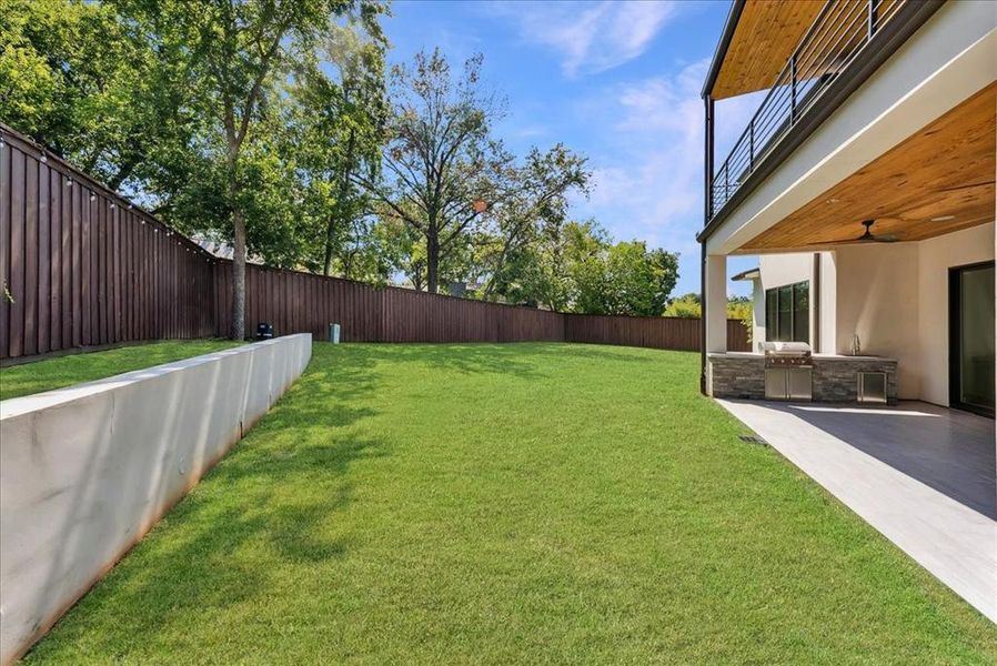 Fenced backyard featuring an outdoor kitchen, a patio area, and a balcony