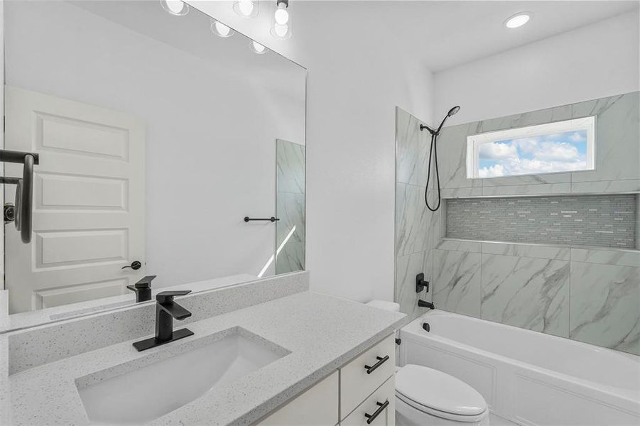 Full bathroom featuring vanity, tiled shower / bath combo, and toilet