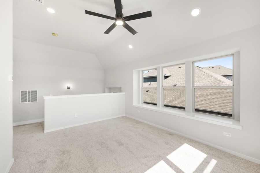 Empty bonus room with vaulted ceiling, black ceiling fan, carpet flooring, and large windows Empty bonus room with vaulted ceiling, black ceiling fan, carpet flooring, and large windows
