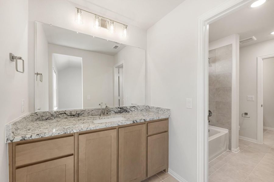 Bathroom with granite vanity, wood cabinets, large mirror, and separate tub and shower area with tile walls.