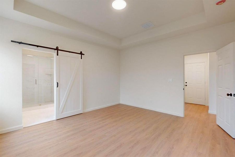 Empty room featuring visible vents, a barn door, baseboards, light wood-style floors, and a raised ceiling