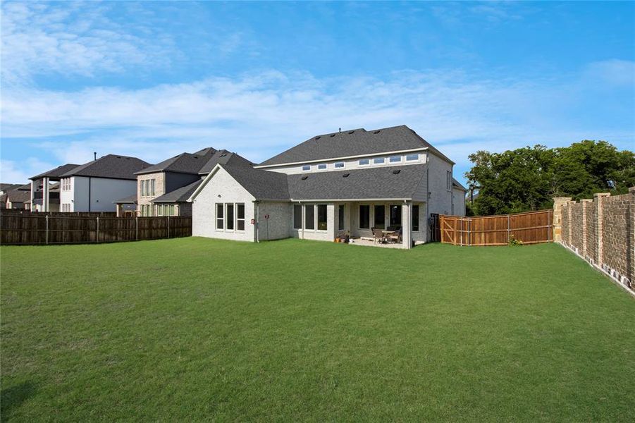 Expansive rear yard featuring a manicured lawn, full privacy fencing, and a covered patio