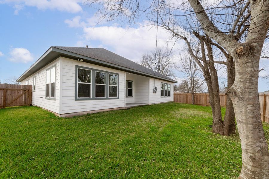 Charming single-story home with white siding and large windows, set in a spacious fenced backyard with lush green grass and mature trees, perfect for outdoor activities.