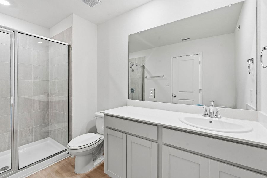 Bathroom featuring a glass-enclosed shower with tile surround, a single vanity with an undermount sink, light-toned cabinetry, a white countertop, and wood-finish flooring Bathroom featuring a glass-enclosed shower with tile surround, a single vanity with an undermount sink, light-toned cabinetry, a white countertop, and wood-finish flooring
