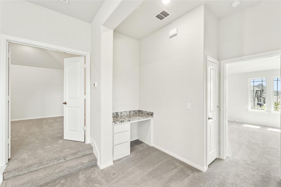 Hallway with built-in desk, granite countertop, white walls, and carpet flooring leading to two rooms