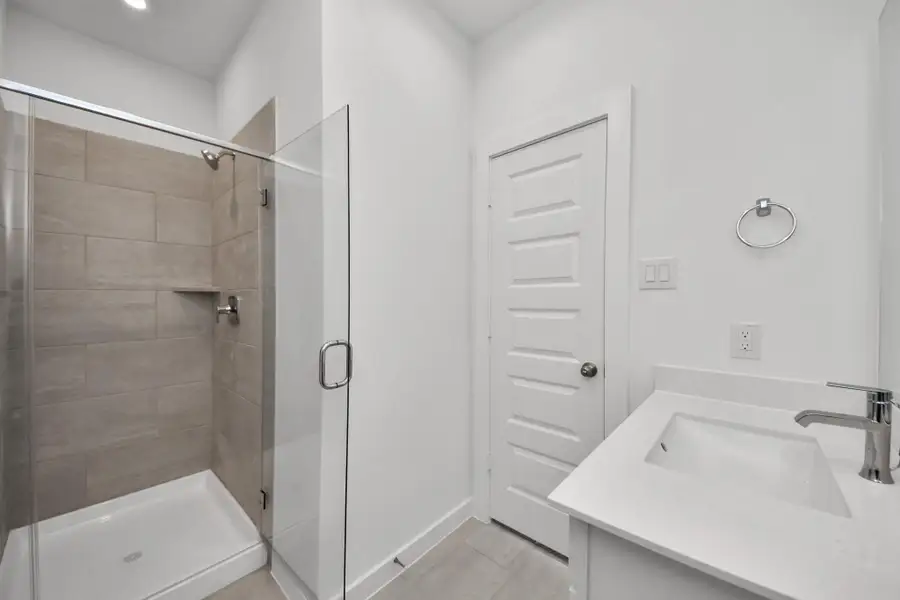 Secondary bath features tile flooring, walk-in shower with tile surround, light stained wood cabinets, beautiful light countertop. Sample photo of completed home with similar floor plan. Actual colors and selections may vary.