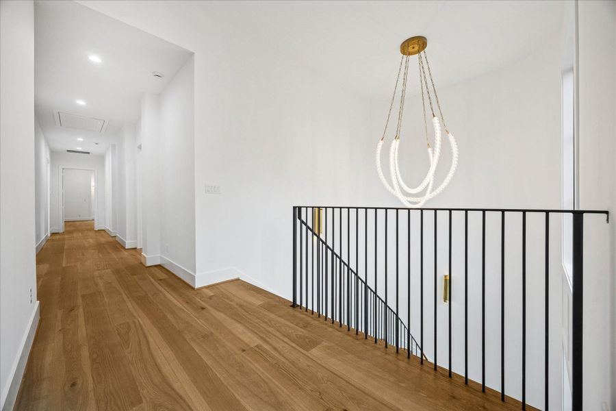 Sculptural lighting and an iron railing define the stair landing. Wide-plank oak floors and 8 ft doors maintain consistency across the second level.