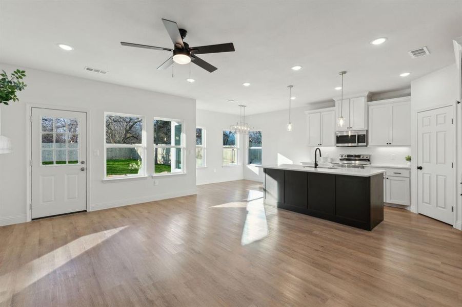 Kitchen with appliances with stainless steel finishes, sink, pendant lighting, a center island with sink, and white cabinets