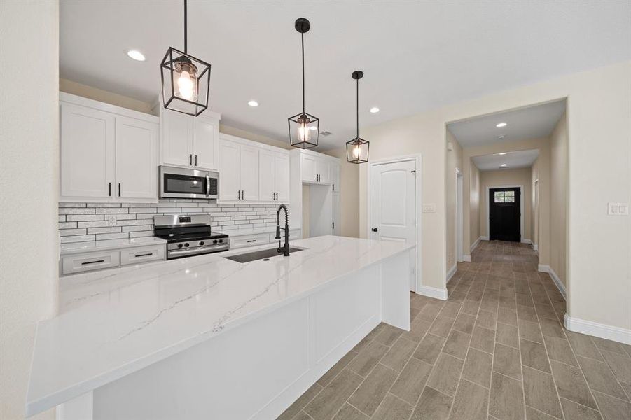 Kitchen featuring backsplash, light stone counters, stainless steel appliances, and white cabinetry