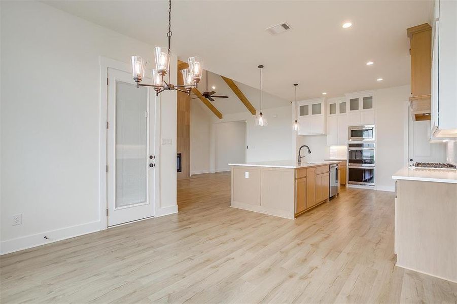 Kitchen with ceiling fan with notable chandelier, a kitchen island with sink, light hardwood / wood-style floors, stainless steel appliances, and vaulted ceiling with beams