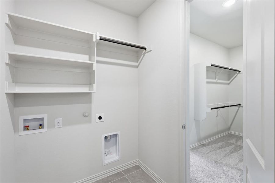 Utility room featuring built-in shelving, a clothes hanging rod, and tile flooring