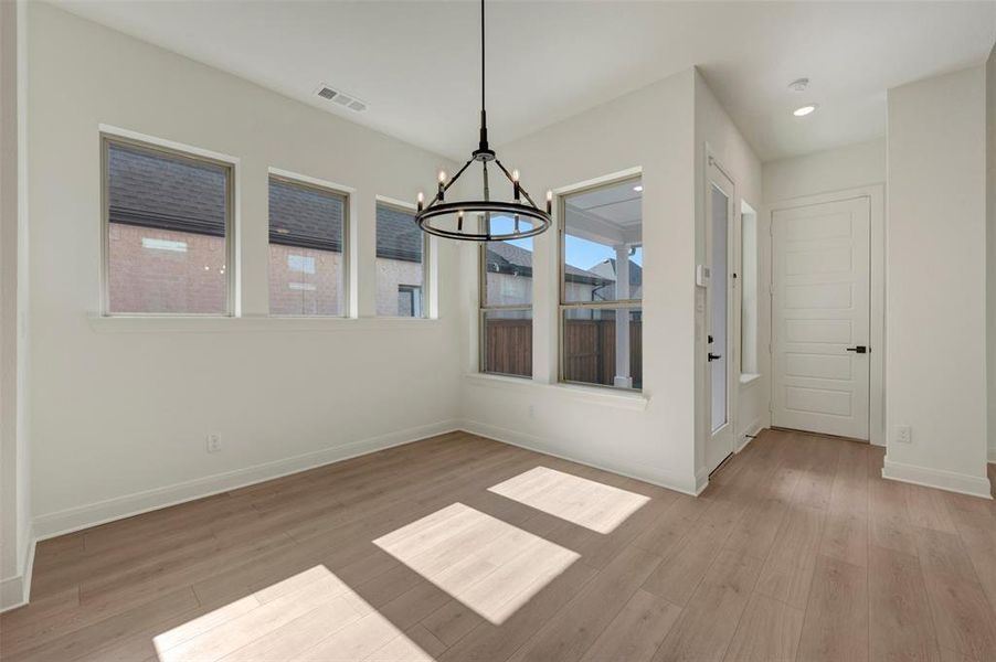 Spacious room featuring multiple windows, wood-finish flooring, a modern chandelier, and a paneled door Spacious room featuring multiple windows, wood-finish flooring, a modern chandelier, and a paneled door