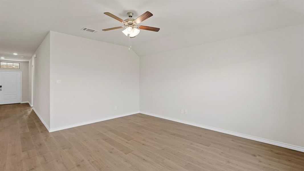Spacious room with wood-finish flooring, a ceiling fan with integrated lighting, recessed lighting, and a white entry door with an overhead transom window