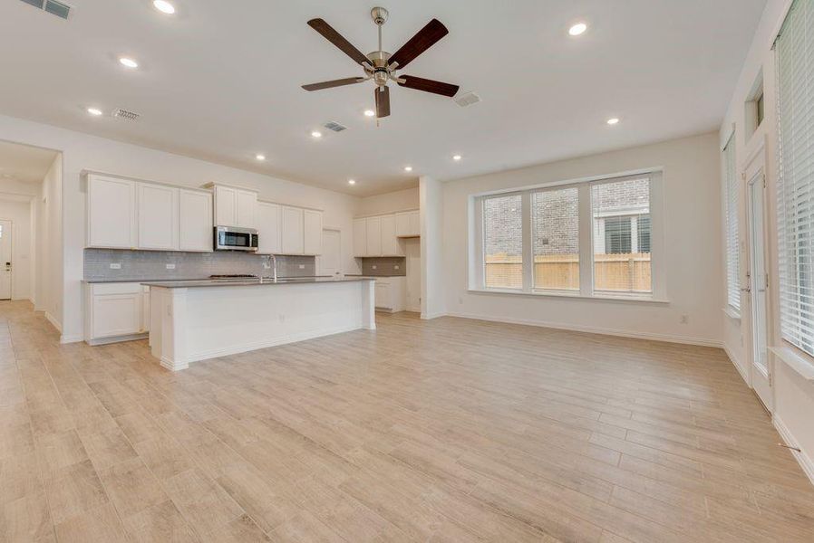 Kitchen with ceiling fan, tasteful backsplash, white cabinets, and a kitchen island with sink