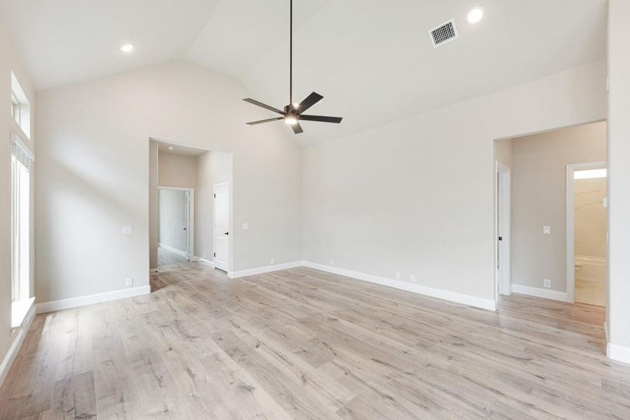 Empty bedroom with vaulted ceiling, ceiling fan, and light wood floors