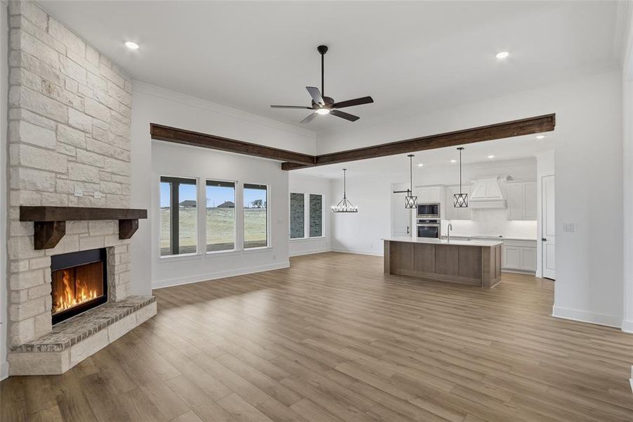 Unfurnished living room featuring a ceiling fan, a fireplace, light wood-style floors, crown molding, and recessed lighting