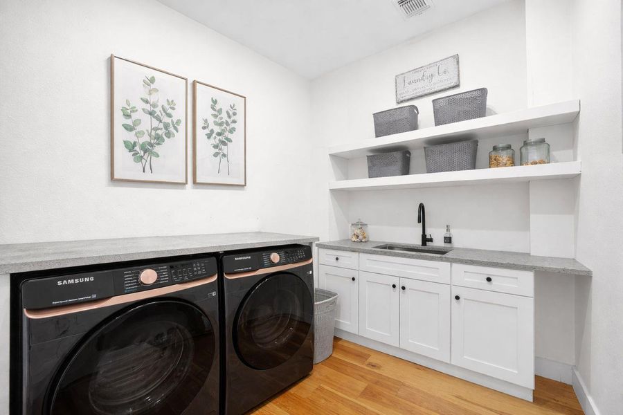 Laundry area with washing machine and dryer, light wood finished floors, and cabinet space