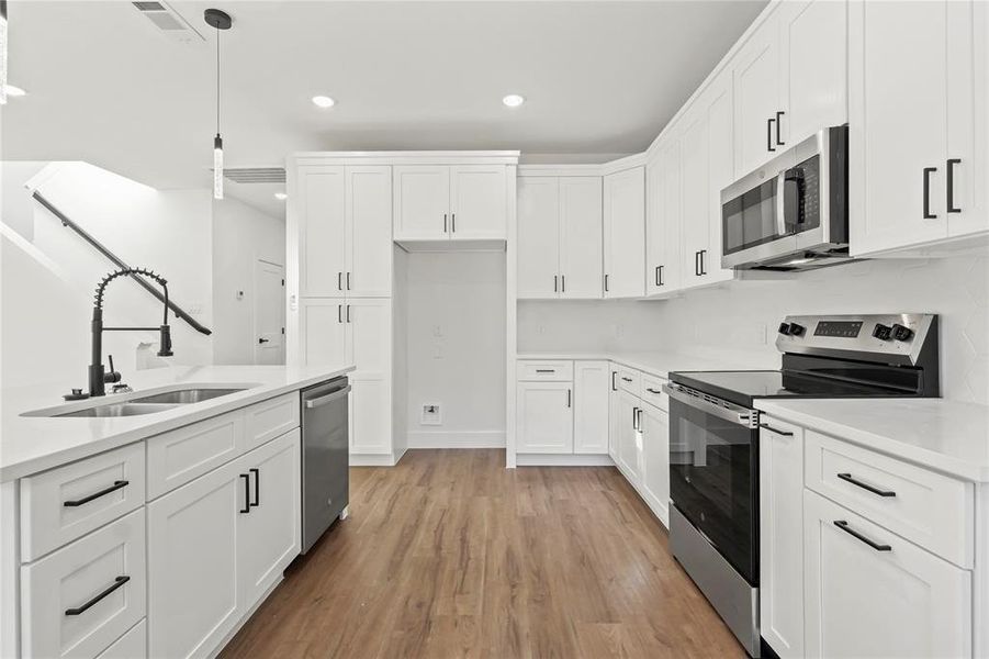 Kitchen with appliances with stainless steel finishes, white cabinets, recessed lighting, light wood-style flooring, and light stone counters