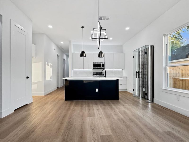 Kitchen with a center island with sink, white cabinetry, dark cabinetry, pendant lighting, and modern cabinets