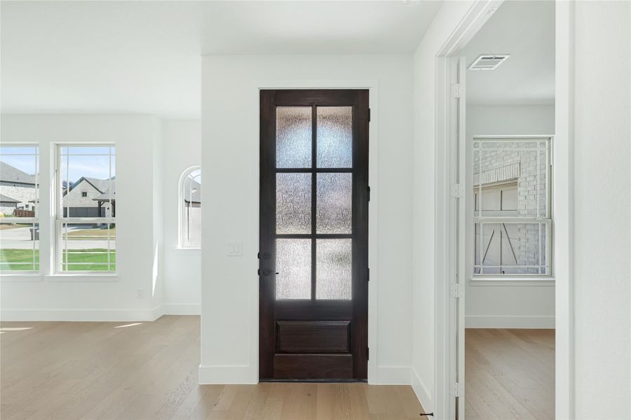 Dark wood interior door with frosted glass panels in a bright white entryway with light hardwood floors