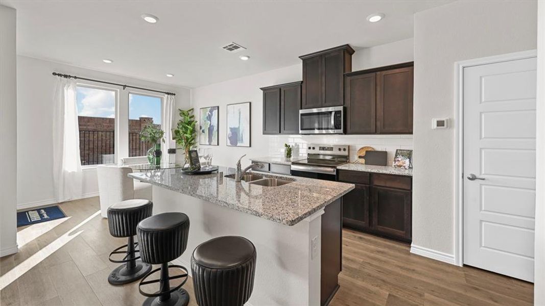 Kitchen featuring tasteful backsplash, light stone countertops, dark brown cabinets, appliances with stainless steel finishes, and a center island with sink Kitchen featuring tasteful backsplash, light stone countertops, dark brown cabinets, appliances with stainless steel finishes, and a center island with sink