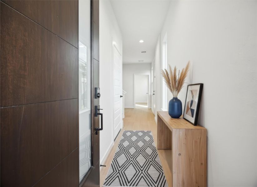 Entryway features a modern aesthetic with LVP light oak–style floors and crisp white trim for a clean, welcoming feel. The open staircase leads to the upper level, and just beyond it, an entry to a guest suite/flex space adds convenience and versatility to the layout. *Virtually staged*