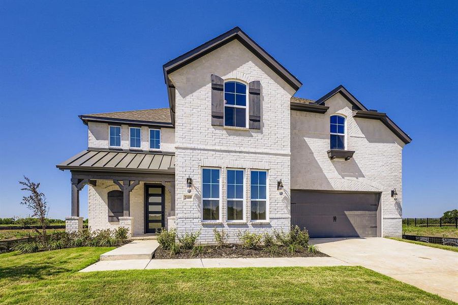 View of front of home featuring a standing seam roof, brick siding, driveway, a metal roof, and a front yard