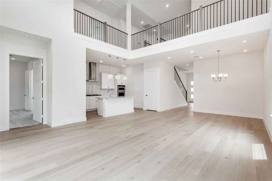 Unfurnished living room featuring light wood-type flooring, sink, an inviting chandelier, and a towering ceiling