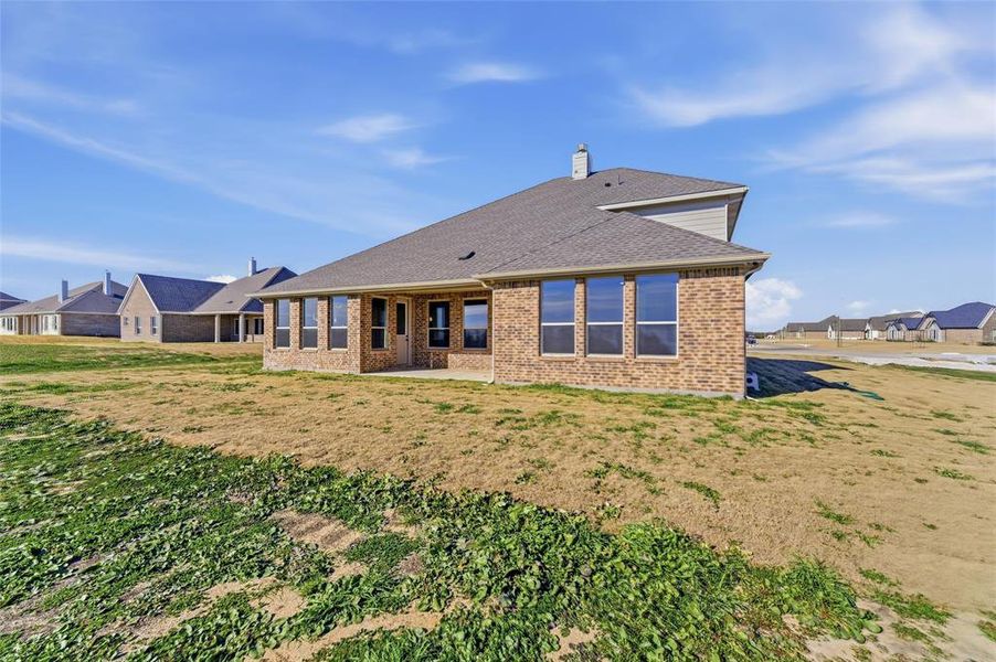 Rear view of house featuring a patio, a yard, a chimney, brick siding, and a shingled roof